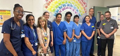 Intensive Care Unit staff standing in a group in front of a wall with a rainbow made of handprints behind.