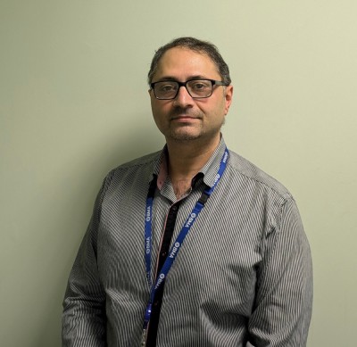 Mr Imad Njam standing in front of a plain beige background.